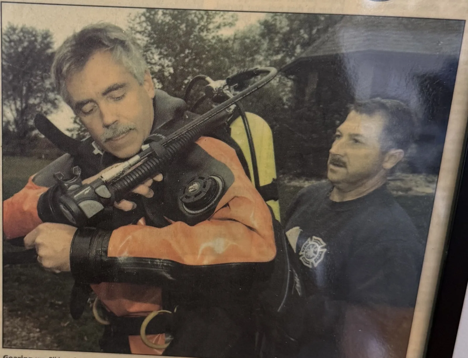 Vito Palumbo in an orange dry suit checking his regulator, with diving instructor Mark Vilmure beside him