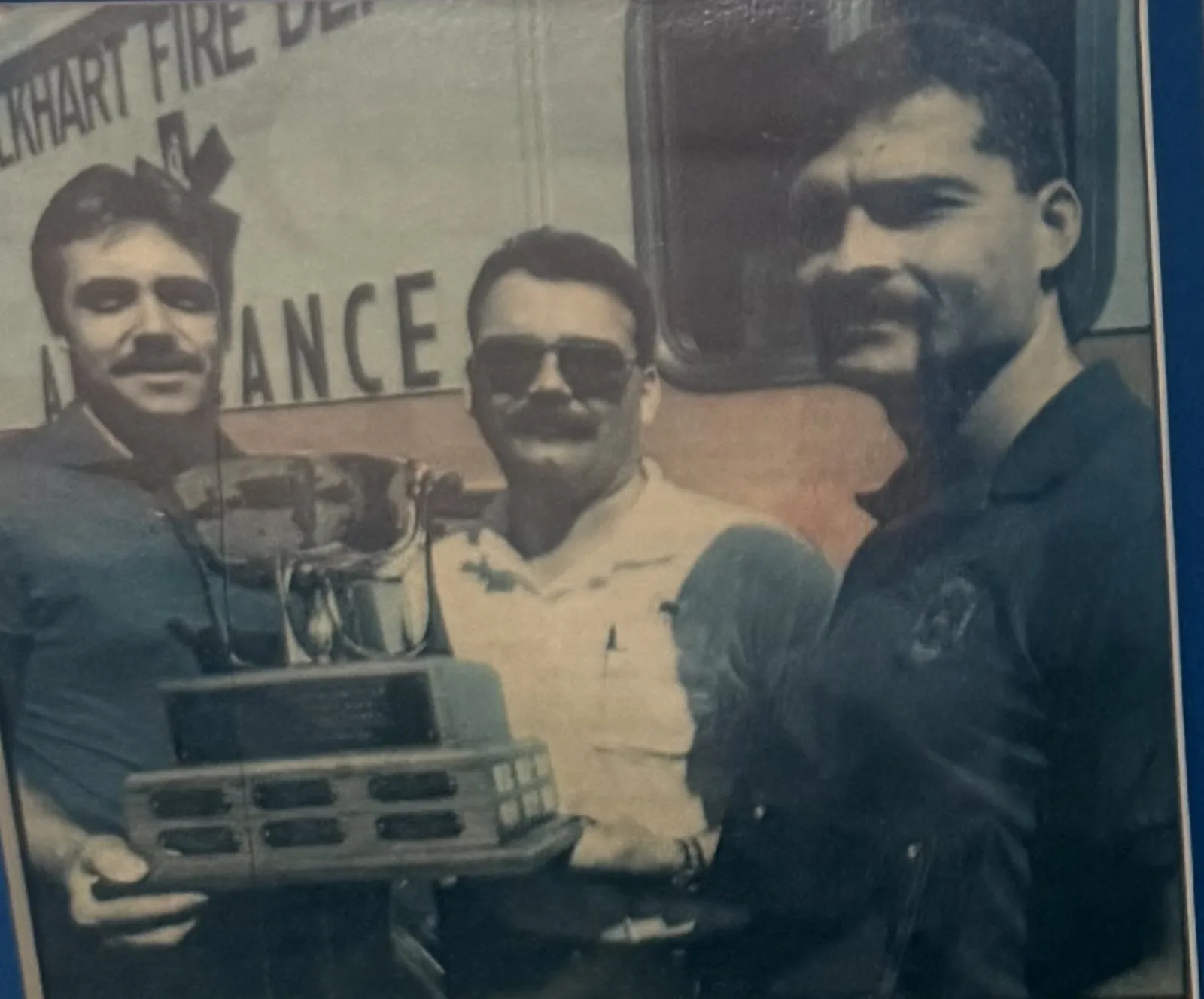 Lt. Vito Palumbo, Chief Paramedic Jay Michael, and Grant Roberts holding the Governor's Cup trophy in front of an Elkhart Fire Department ambulance, 1993